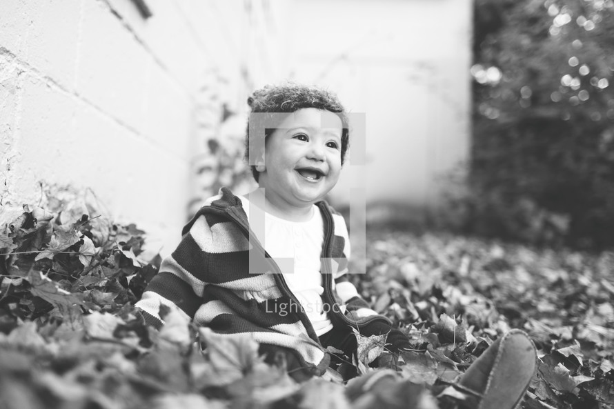 Smiling toddler boy sitting in the leaves