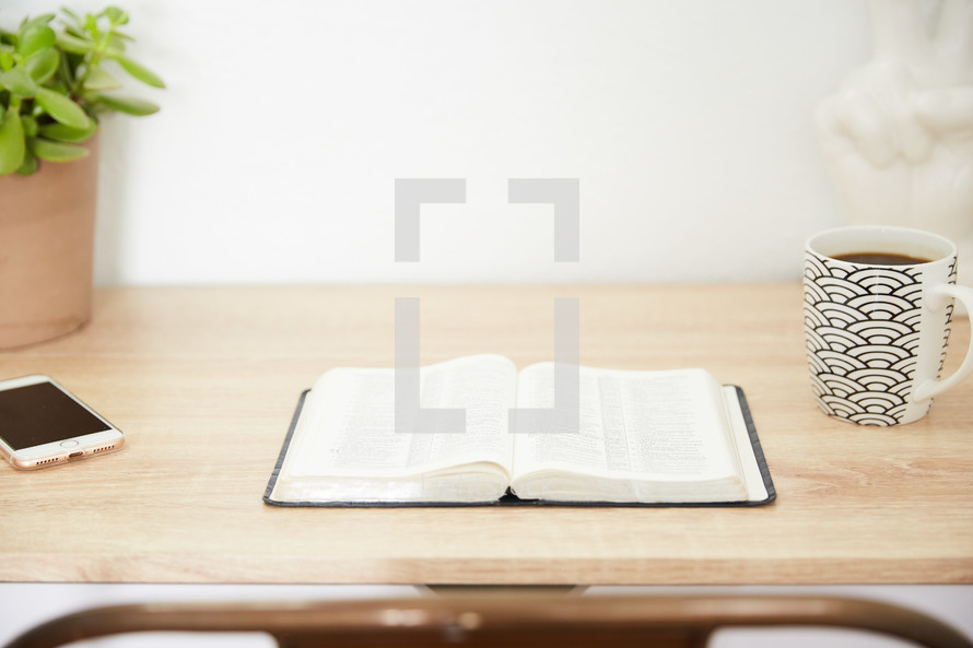 an open Bible and cellphone on a wood desk 