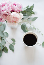 pink peonies in a vase and leaves on a desk with coffee mug 