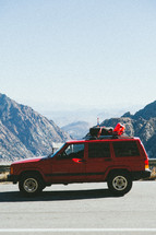 a red SUV parked on the side of the road and view of mountains 