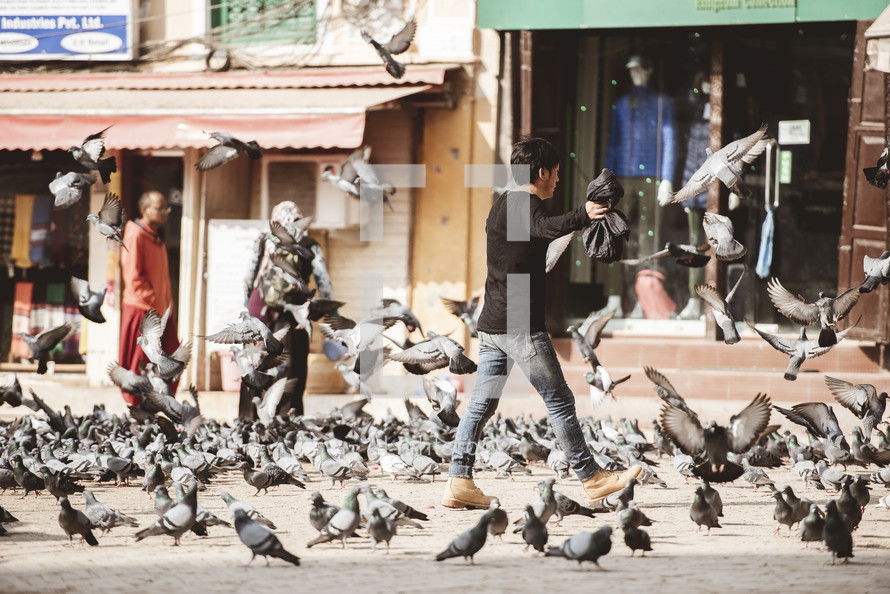 man chasing off pigeons in Tibet