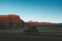 a SUV parked on the side of a road and view of red rock cliffs 