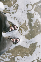 a man in sandals standing in shallow ocean water 