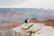 people sitting on the edge of a cliff looking out over a canyon 
