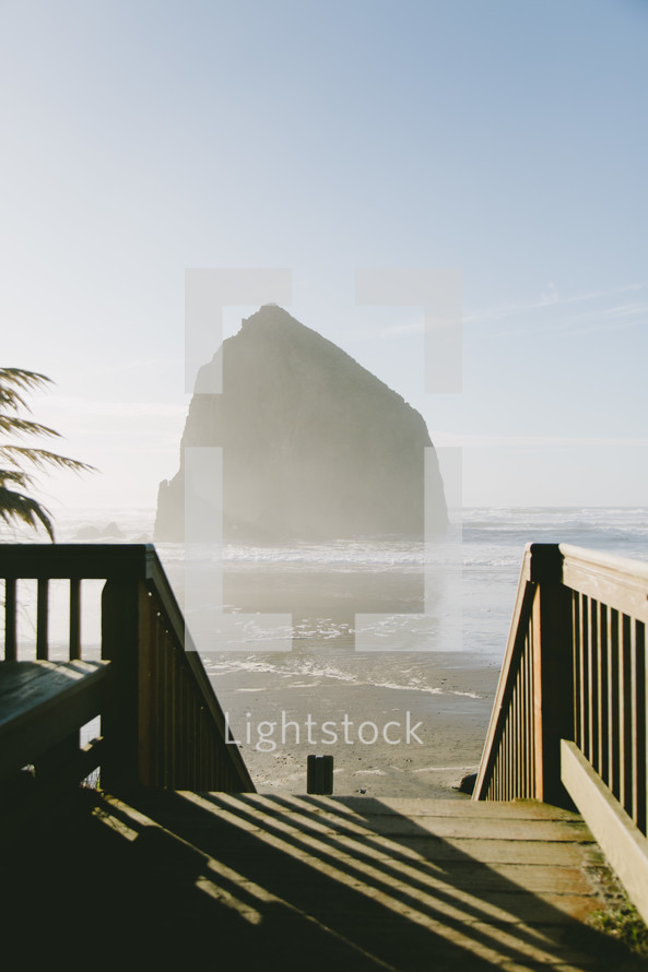 wooden steps to a beach and view of a rock formation in the ocean 