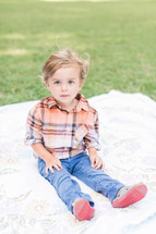 a little boy sitting on a blanket in the grass 