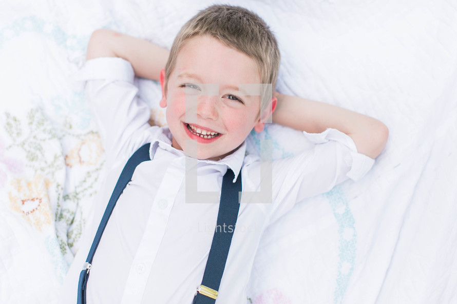 a little boy in suspenders relaxing on a blanket 