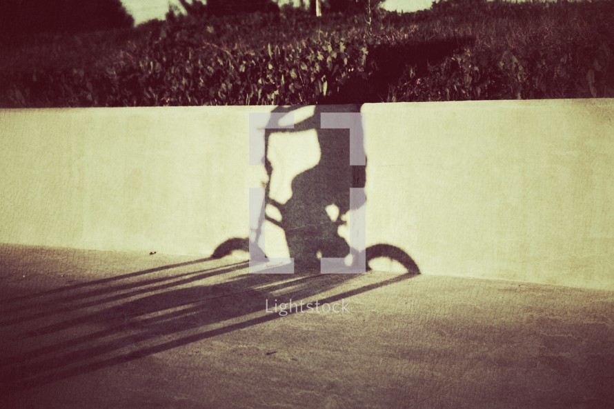 The shadow of a young boy riding his bicycle on the sidewalk