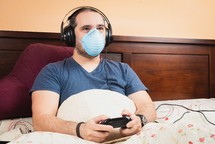 sick man with headphone and medical mask, playing videogames in the bed