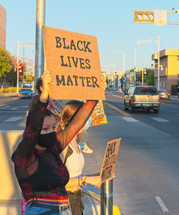 young women standing on a sidewalk holding up Black Lives Matter signs 