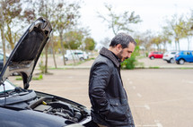a man standing next to a car with engine trouble 