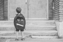 a boy standing in front of school doors 