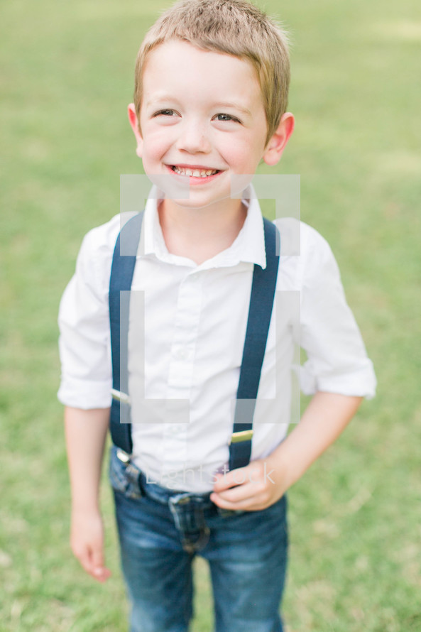 a smiling boy child in jeans and suspenders 