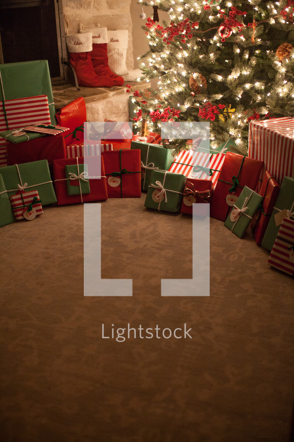 gifts under a Christmas tree and stockings by a fireplace 