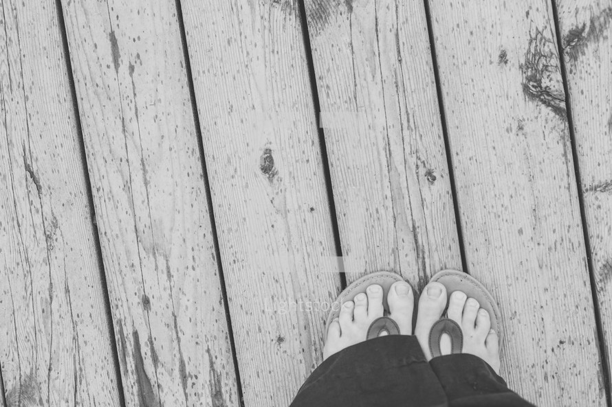 feet in flip flops standing on a dock 
