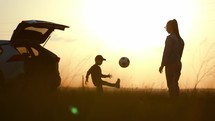 Mom and son play on ball near a car with an open trunk at sunset. A happy family. Silhouette of a family in the summer sun. Concept of friendly family. Family vacation in nature.