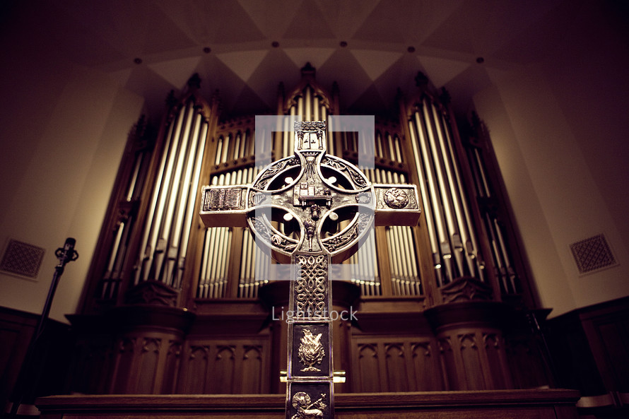 cross on an altar in front of organ pipes