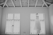 A wedding dress hanging by a window in a white room