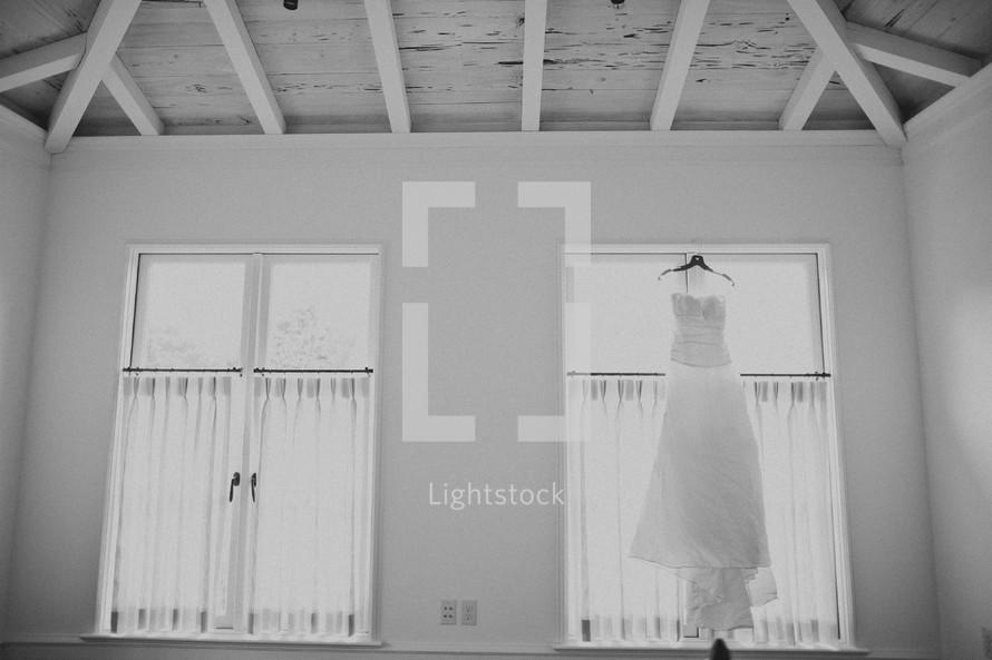 A wedding dress hanging by a window in a white room