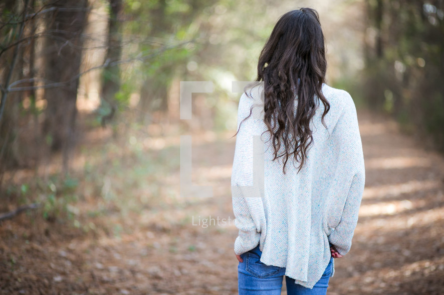 woman in a sweater walking on a path in a forest 