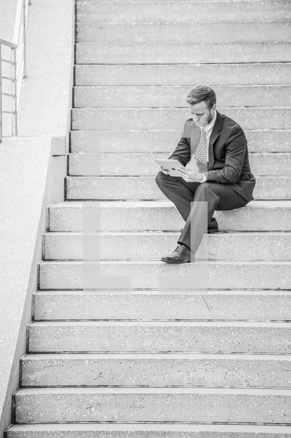 a businessman with a tablet sitting on steps 