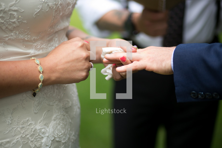 A bride placing a ring on the groom's finger during a wedding ceremony.