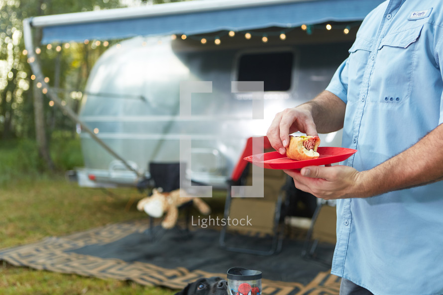 a man carrying a hotdog on a plate in front of a camper 