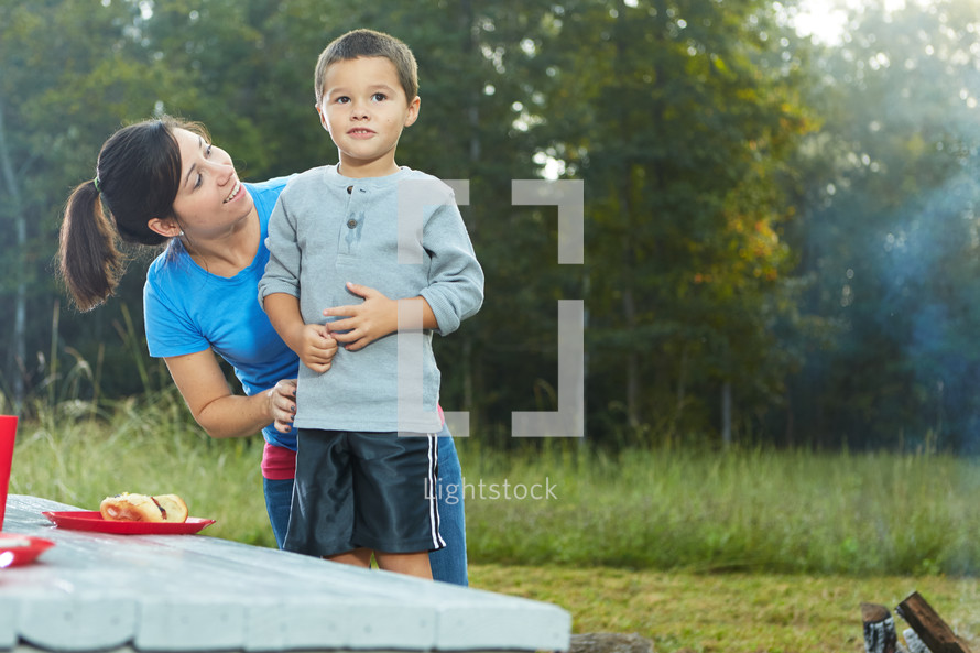 mother and son eating hotdogs at a picnic table 
