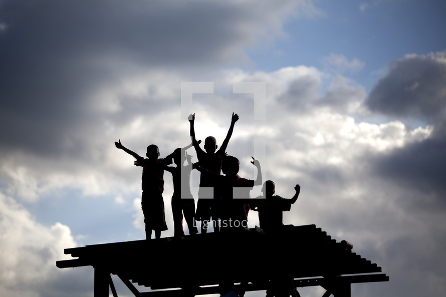 Silhouette of children with arms raised on top of platform.