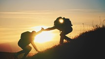 Silhouette of a helping hand to the man mountaineer. Two hikers on top of the mountain, a man helps a man to climb. Two hiker helping on hiking trail to summit the top of mountain. Teamwork concept.