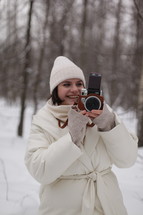 a woman holding a camera standing in snow 