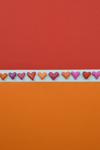 hearts in a row as ribon on white between orange and red paper with copy space above and below as sign for love and relationship or emotions