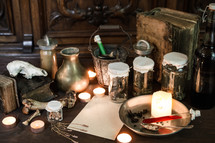 vintage Apothecary - or:
eerie witches' kitchen with lot of ingredients for a potion, a blank sheet of paper for the recipe or greetings and ancient gruesome jars dark with only candlelight for Halloween