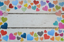 colorful paper hearts on a white wood background - frame of multicolored paper hearts on a weathered white wooden background 
