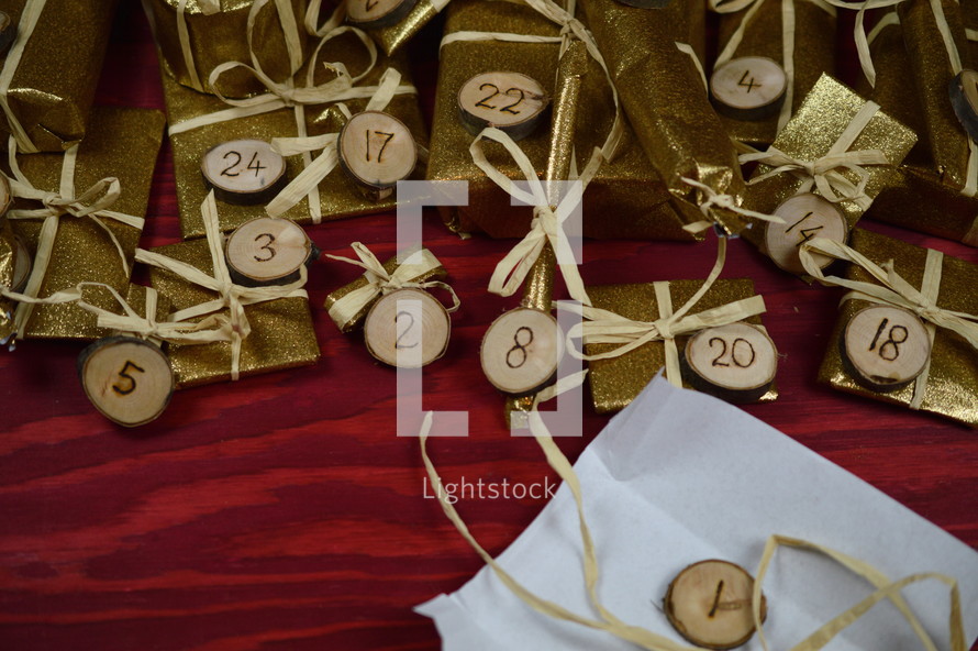 advent calendar with twenty four golden presents on red wood with the numbers burned into round wood pieces and the first present unwrapped