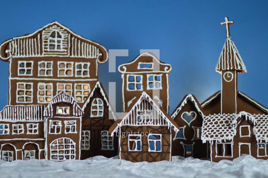 home made gingerbread village in front of blue background on white snowlike velvet as advent decoration