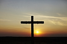 The sun goes down on a cross erected on a hillside.