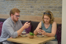 a couple sitting at a table together texting on their phones 