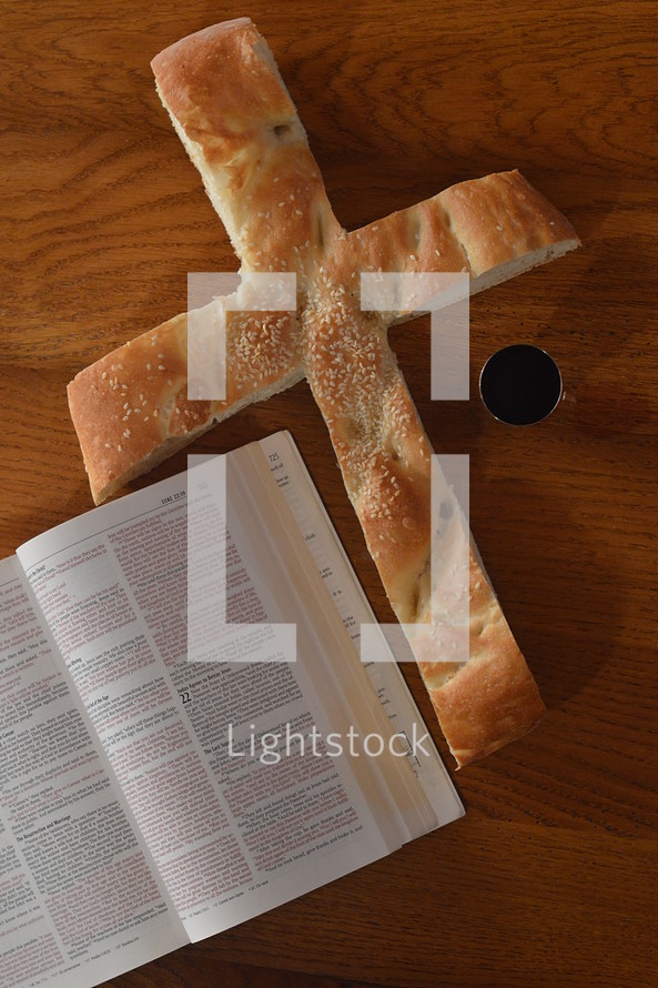 Bread in the shape of a cross with an open bible and a goblet of wine. 
