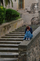 a sad young woman sitting along on concrete steps 