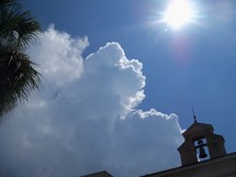 The Heavens roll away like a curtain revealing the glory of God. Clouds covering a bell tower on a sunny day.