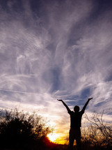 silhouette of a man at sunset with raised hands 
