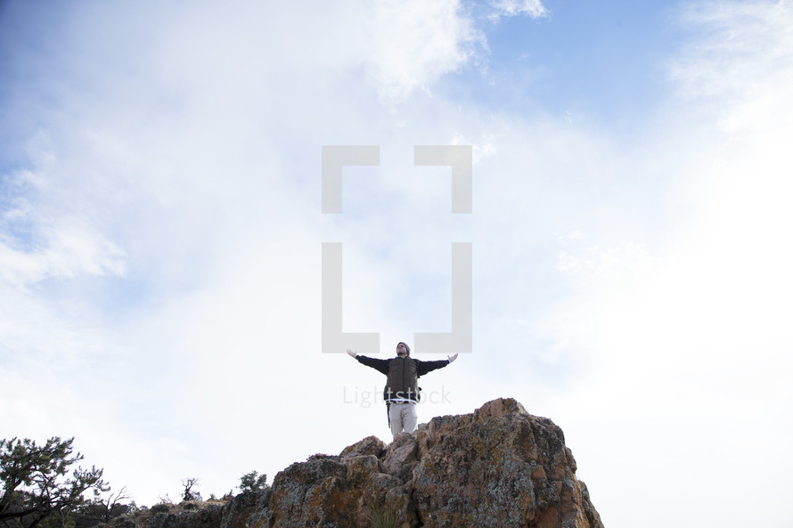 a man standing at the top of a cliff with open arms 