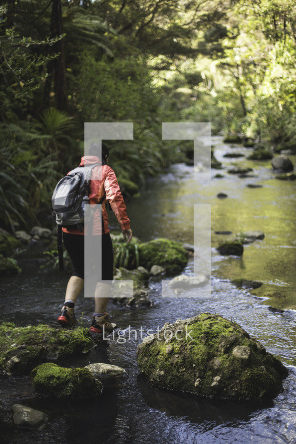 man backpacking across moss covered rocks in a river 