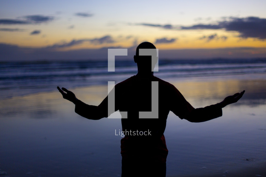 silhouette of a man in worship on a beach 