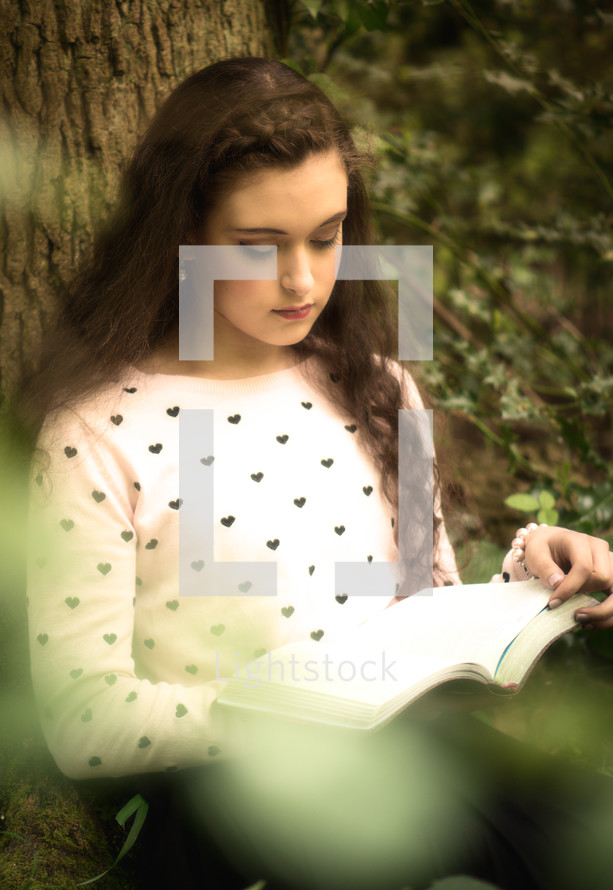 a young woman reading a book under a tree 