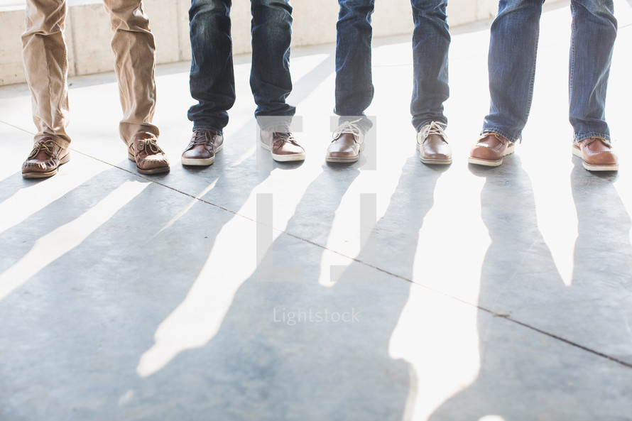 feet and shadows of men standing on a sidewalk.