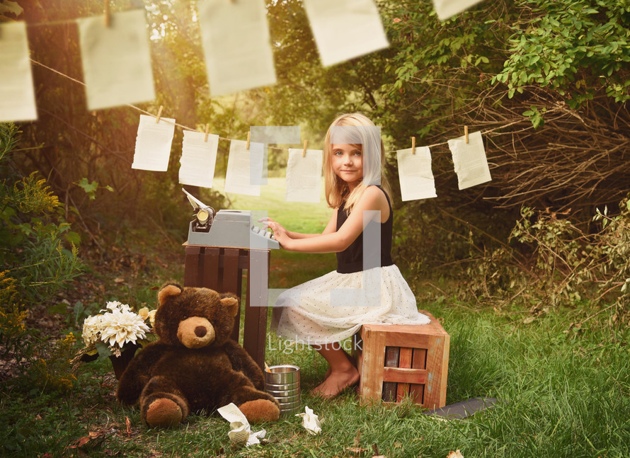 a little girl typing on a typewriter outdoors and pages hanging on a clothesline 