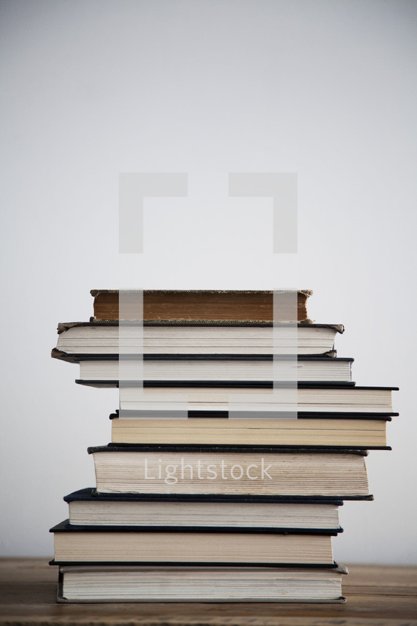 A tall stack of books on a wooden table.