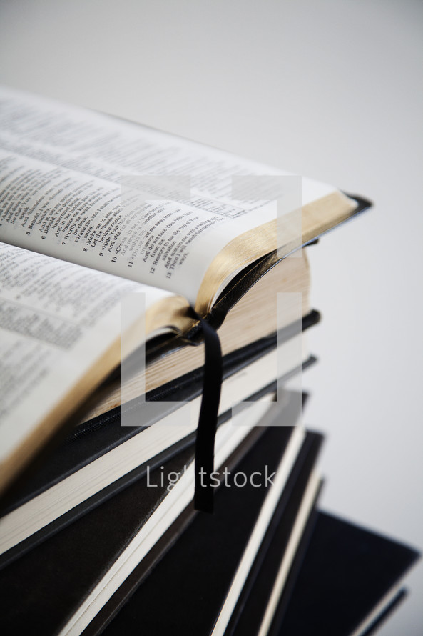 An open Bible on top of a stack of hardback books.